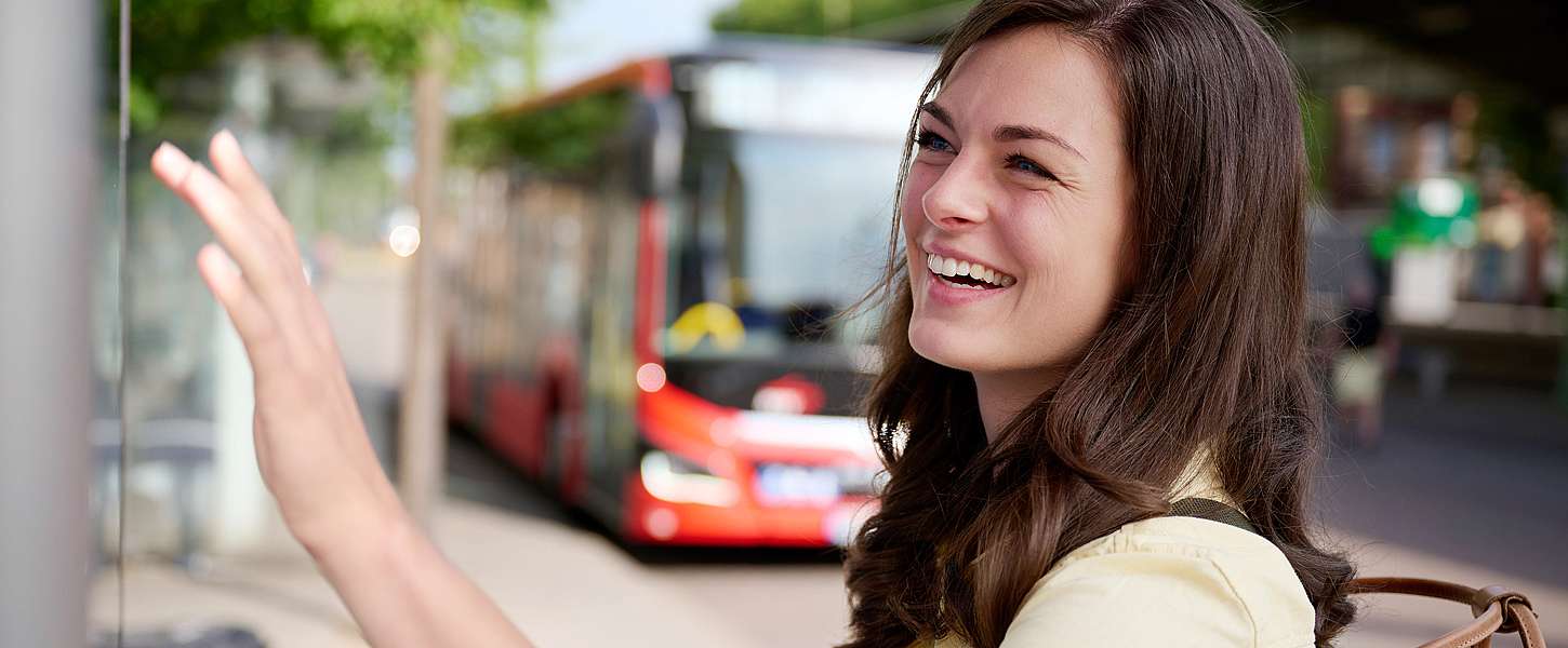 Eine junge Frau steht an einer Haltestelle am Fahrkartenautomat.