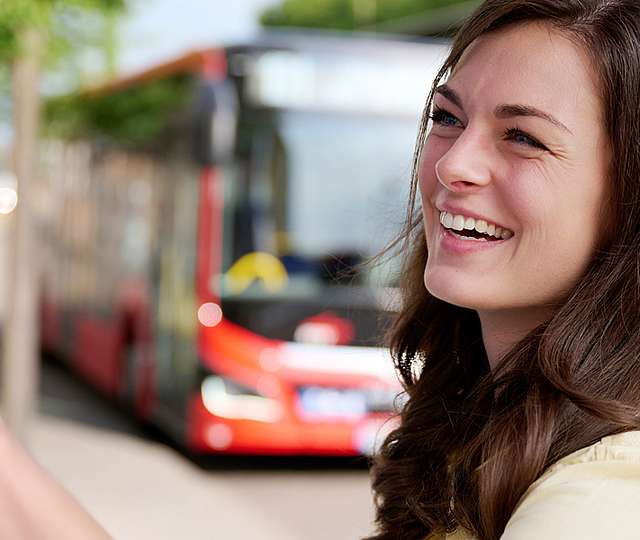 Eine junge Frau steht an einer Haltestelle am Fahrkartenautomat.