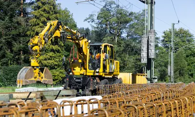 Symbolbild von Infrastrukturarbeiten im Murgtal. Das Foto zeigt einen gelben Bagger. Im Vordergrund stehen Baumaterialien.