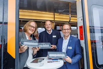 Das Foto zeigt drei Personen in der geöffneten Tür einer Tram-Train-Bahn. Abgebildet sind von links nach rechts Sonja Wiesholzer (Schiene Oberösterreich), Karsten Nagel (Saarbahn) und Christian Höglmeier (Albtal-Verkehrs-Geselllschaft/Verkehrsbetriebe Karlsruhe). Alle halten ein graues Fahrzeugmodell einer Bahn in der Hand. 